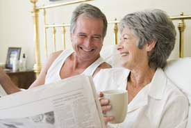 Older couple reading the newspaper and laughing in bed